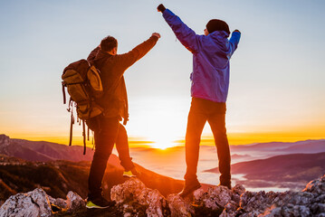 Two happy friends hikers standing with arms up on the mountain top during the hiking concept of...