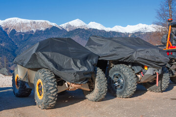 Shelter with a protective cover with a tarpaulin off-road vehicles stand against the backdrop of snow-capped mountains.
