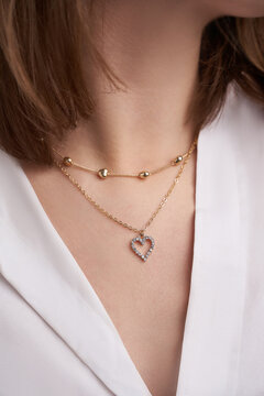Close-up shot of a young woman's neck. She is adorned with an exquisite double necklace of yellow jewelry alloy with a large heart-shaped pendant decorated with sparkling clear crystals.
