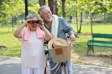 Portrait of happy asian senior man and woman walking and hugging with bicycle and binoculars in summer garden outdoor. Lover couple going to picnic at the park. Happiness marriage lifestyle concept.