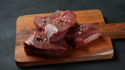 Fresh meat on wooden cooking board on dark background. Few pieces of raw meat