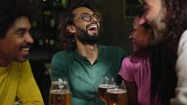 Group of diverse friends enjoying weekend together cheering with beers at brewery bar - International friendship concept