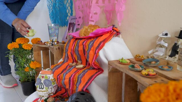 Mexican lady looking for a place to put a clay vase to decorate an altar for the day of the dead. Altar of d&iacute;a de muertos full of skulls, ofrendas, tequila, cempas&uacute;chil flowers, food and papel picado
