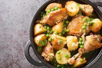 Italian American cuisine Chicken Vesuvio a skillet with potatoes, garlic, green peas closeup on the black pan on the table. Horizontal top view from above