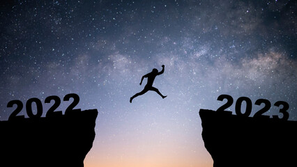 Silhouette of young businessman jumping over a cliff from 2022 to 2023 with star and Milky Way over on the sky. Concept of planning, goal, challenge, new year resolution.