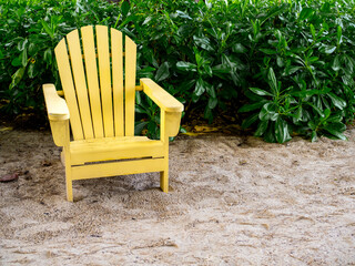 An empty yellow wooden sun chair on the sand beach on green leaves background with copy space. Wood...