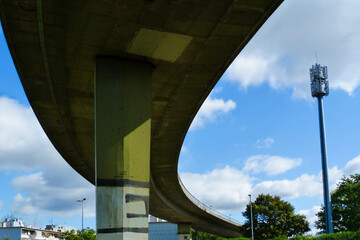 concrete overpass highway underside view with heavy column. low angel view. street lights and blue sky with white clouds. curving high speed road. transportation concept. diminishing perspective