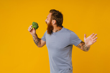 Bearded man holding broccoli while standing isolated over background