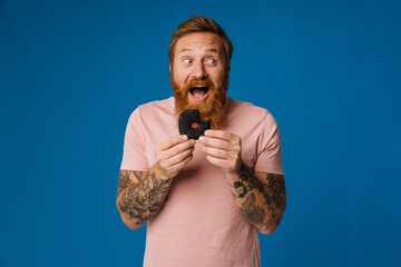 Bearded man holding donut while standing isolated over blue background