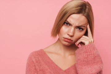 Pensive blonde woman touching her temple isolated over pink background