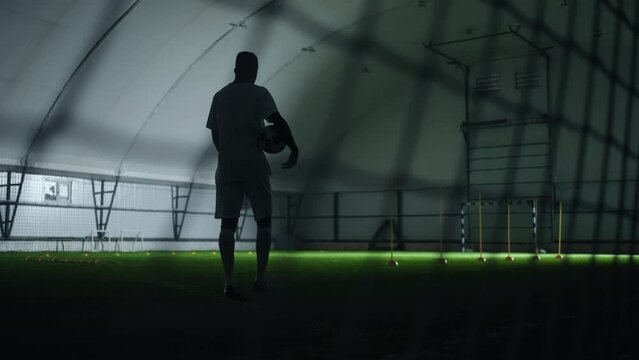 exhausted footballer walking alone on football pitch indoors after training, epic slow motion shot