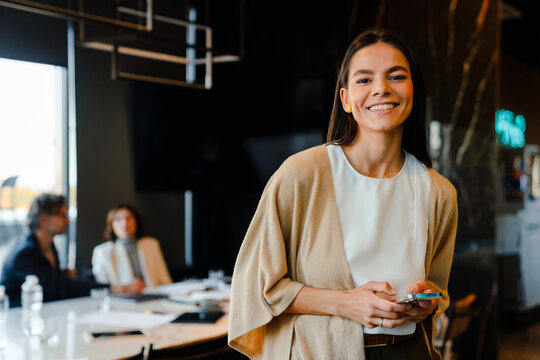 Hispanic Young Woman Smiling And Using Cellphone During Offline Meeting