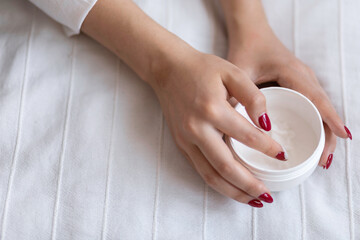 Beautiful groomed woman's hands with cream jar on the blanket. Moisturizing cream for clean and soft skin. Healthcare concept.