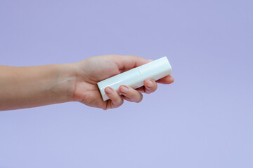 Womans hand holds a white tube (cream battle) for cosmetic products isolated on lilac background