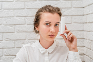 Woman recomending you cosmetic product with white brick wall background. Cosmetics, beauty and spa...
