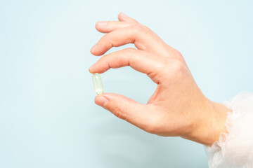 Doctor's hand holding a fish oil capsule (Omega 3) or pill isolated on light blue background