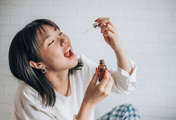 Asian woman dripping cbd oil into her mouth. Close up asian women taking CBD Oil for sleep. Medical...