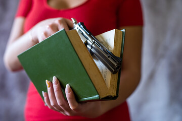  girl in a red dress pulls  handgun in book isolated on grey