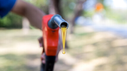 Gas nozzle with one last drop. Orange gasoline nozzle on nature background. Refill and filling Oil...