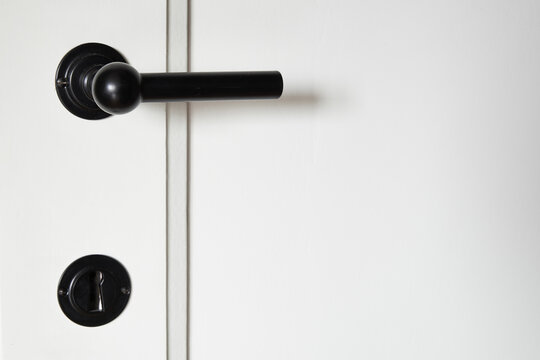 Black metal door handel on white wooden door