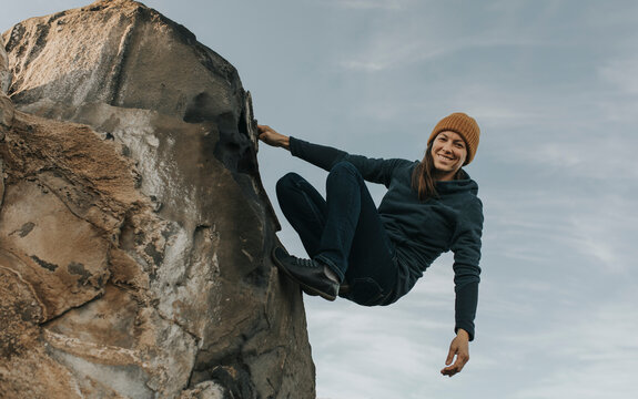 Happy woman climbing rock in front of sky