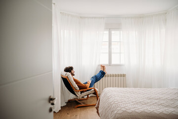 Young man relaxing on armchair in bedroom at home