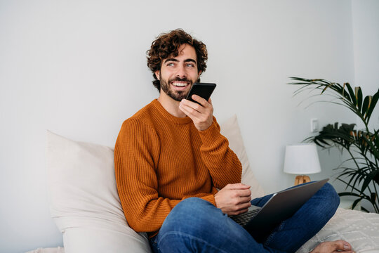 Happy freelancer sending voicemail through smart phone at home