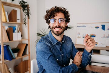 Cheerful young engineer wearing eyeglasses holding pen in office