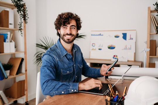 Smiling young engineer sitting with laptop in office