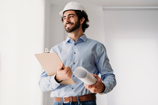 Happy engineer wearing hardhat holding blueprints in office