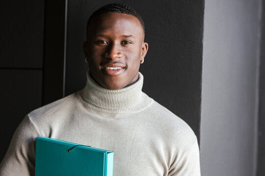 Smiling businessman with file folder in front of wall