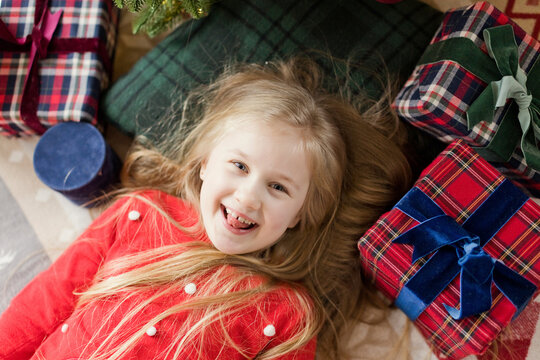 Cheerful girl lying on rug with Christmas gifts at home