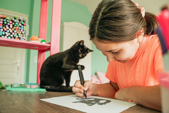 Girl drawing cat picture on paper at home