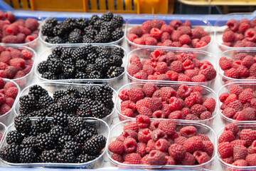 Freshly picked organic strawberries, blackberries, raspberries, currants in plastic transparent trays on the market. Summer ripe juicy berries, eco-friendly product, healthy food