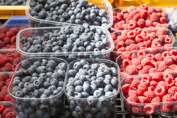 Freshly picked organic strawberries, blackberries, raspberries, currants in plastic transparent trays on the market. Summer ripe juicy berries, eco-friendly product, healthy food