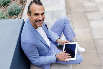Happy mature businessman with tablet PC sitting on bench