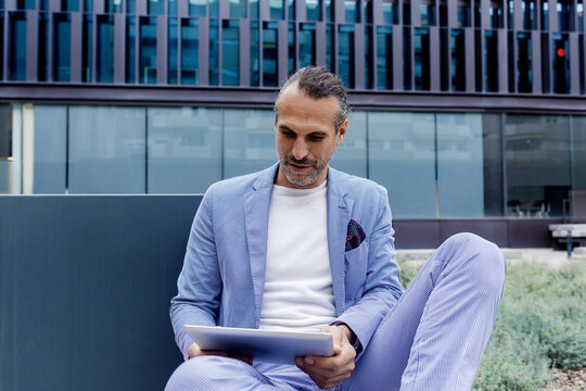 Mature Businessman Using Tablet PC Sitting On Bench Outside Office Building