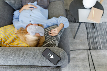 Woman wearing eye mask sleeping on sofa with smart phone at flight mode