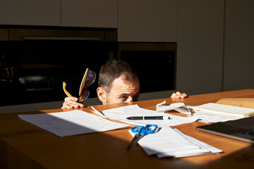 Worried man hiding from financial bills on desk at home