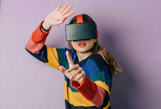 Girl wearing VR simulator gesturing against purple background
