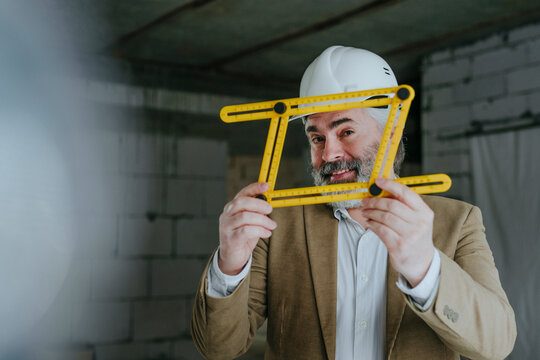 Architect looking through four-fold adjustable ruler at under construction site