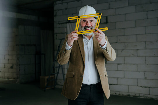 Happy architect looking through four-fold adjustable ruler at under construction site