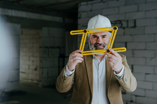 Smiling architect wearing hardhat looking through four-fold adjustable ruler