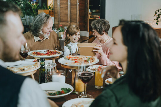 Happy Girl Giving Gift Gift To Grandparents At Cafe