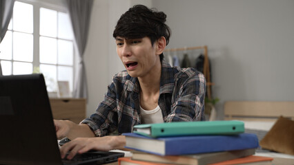 stressed asian Japanese man working from home is rubbing face and scratching head while having an emotional breakdown over the crashed computer while in the bedroom