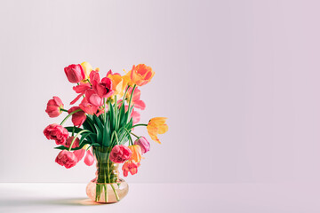 Big flowers bouquet of multicolored tulips in vintage glass vase on pink color background with copy space. Business card. Invitation postcard. Place for greeting text. International holiday. Banner