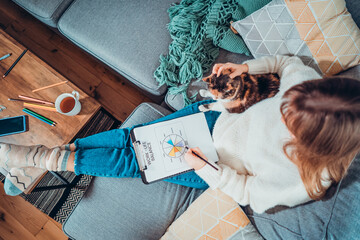 Top view relaxed young woman drawing work-life balance wheel sitting on the sofa with cat pet at...