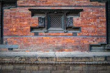 Fototapeta na wymiar Frontal view of a traditional Nepalese temple facade with red bricks and ornamental carvings. A closed wooden window made of dark wood.
