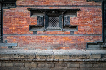 Frontal view of a traditional Nepalese temple facade with red bricks and ornamental carvings. A closed wooden window made of dark wood.