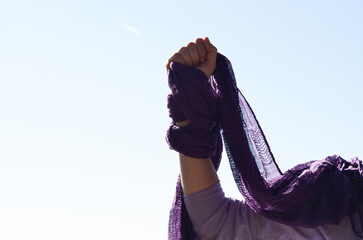Feminist woman's fist grabbing a lilac scarf. Blue sky. Concept of fighting for women's rights....